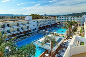 Un hotel con múltiples piscinas, una terraza en la azotea y vistas del paisaje circundante.