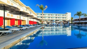 Ein Schwimmbecken mit Liegestühlen und Sonnenschirmen, umgeben von einem mehrstöckigen Hotelgebäude mit Balkonen.