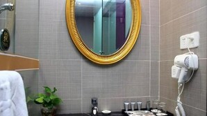 A bathroom with a round mirror, a sink, a hairdryer, and toiletries. - Gentleman Hotel (Shenzhen)