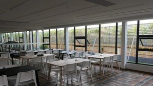 A spacious indoor area with tables and chairs arranged for dining, large windows offering views of an outdoor garden, and a modern ceiling design. - Gentleman Hotel (Shenzhen)