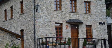 A stone building with a balcony, a sign reading "Casa de Ponte", and a small garden area with potted plants.