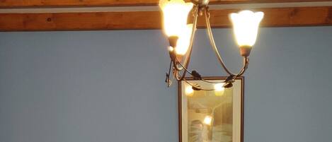 Quarto com duas camas de madeira, uma mesa de cabeceira, um abajur, um candelabro e um quadro na parede.