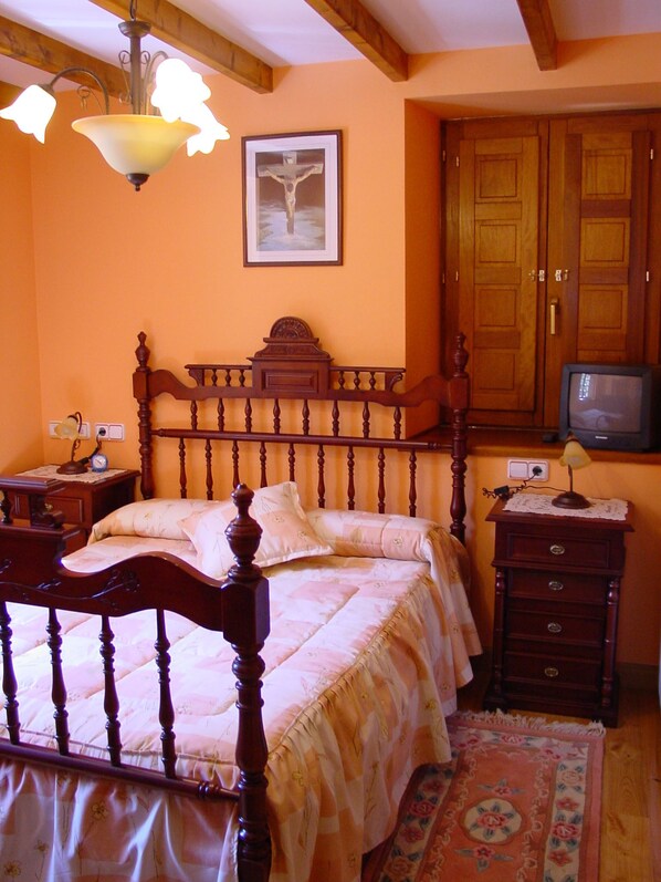 Een slaapkamer met een houten bed, een nachtkastje met een lamp, een ingelijst schilderij aan de muur en een televisie op een standaard.