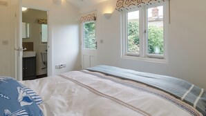 A bedroom with a bed, a window with a view of greenery, a door leading to a bathroom, and a ceiling with exposed beams. - 2 bedroom accommodation in Blakeney (Blakeney)