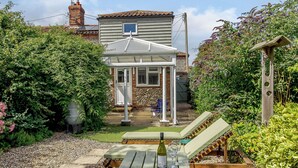 A patio with a wooden table, a bottle of wine, and two glasses. - 2 bedroom accommodation in Blakeney (Blakeney)