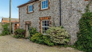A stone building with two windows and a door, surrounded by gravel and greenery. - 2 bedroom accommodation in Blakeney (Blakeney)