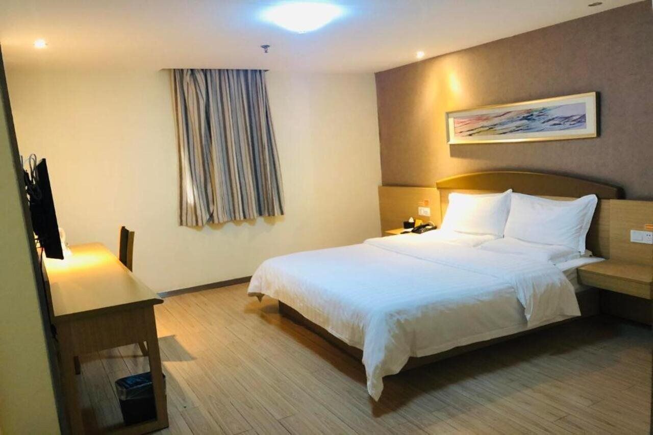 Una habitación de hotel con cama, mesita de noche, lámpara y un cuadro en la pared.