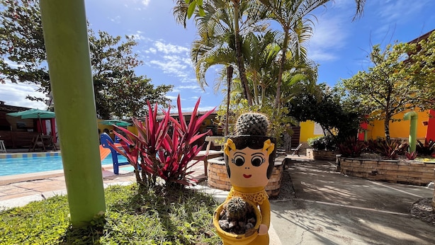 Una estatua de una mujer sosteniendo un cactus, rodeada de follaje y una zona de piscina.