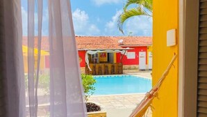 Habitación con vista a una piscina, una hamaca y un edificio rojo con techo de tejas.