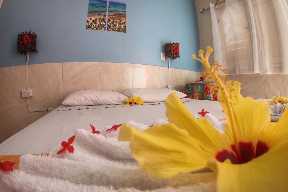 A hotel room with a bed, pillows, a nightstand, a picture on the wall, and a window with curtains.