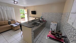 Cocina compacta con isla integrada, un refrigerador pequeño y un comedor con sofá.
