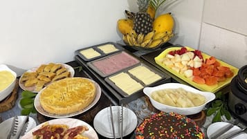A buffet with various food items, including a cake with colorful sprinkles, a plate of sliced meat, and a bowl of fruit.