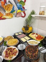 Um buffet com diversos alimentos, incluindo um bolo com confeitos coloridos, um prato de carne fatiada e uma tigela de frutas.