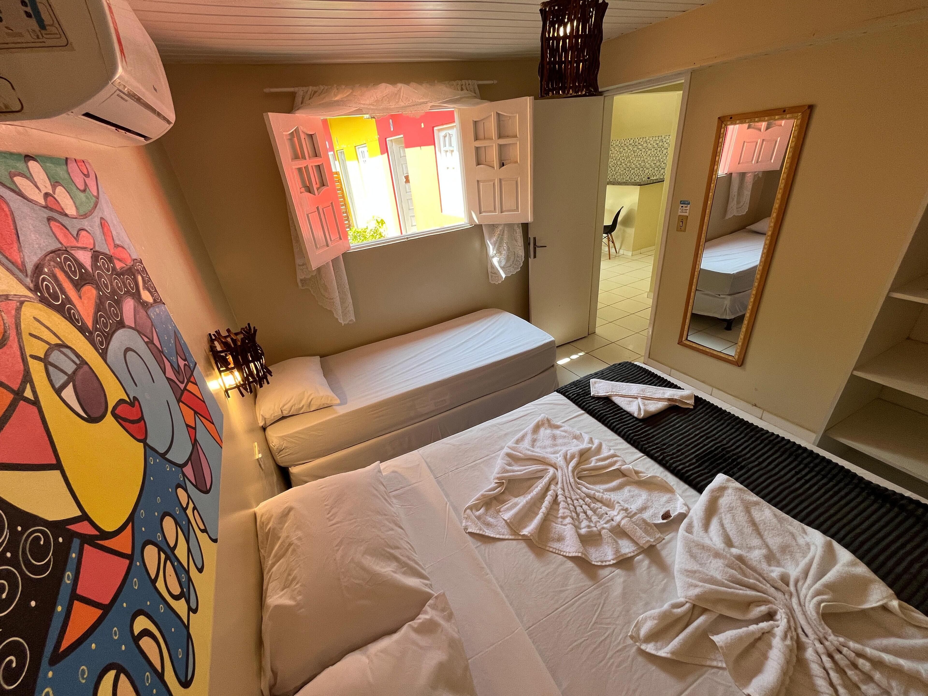 A hotel room with two beds, a large mirror, and a colorful mural on the wall.