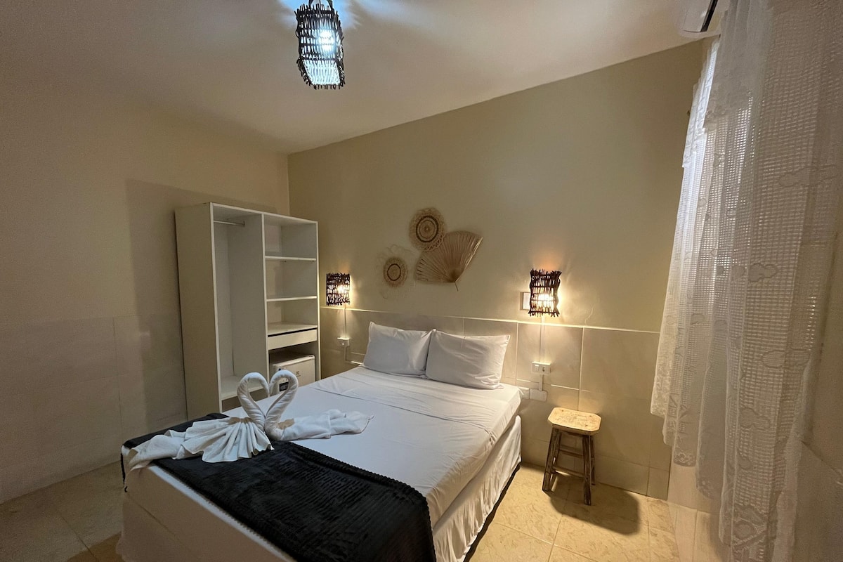 A hotel room with a bed, a wardrobe, a small stool, and decorative wall lights.
