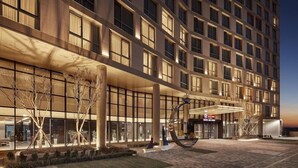 Un hôtel moderne doté d’une grande façade en verre, d’une entrée abritée et d’un espace paysager agrémenté d’arbres et d’une sculpture.