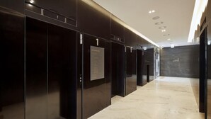 Un couloir moderne avec des portes d’ascenseur noires, un sol en marbre et un plafond doté d’un éclairage encastré.