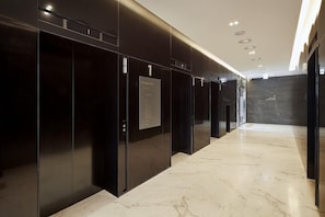 Een moderne gang met zwarte liften, een marmeren vloer en een plafond met inbouwverlichting.