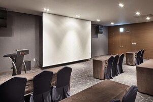 A conference room with a large screen, a podium, and multiple tables with chairs.