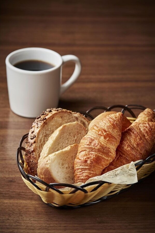 A basket of croissants and a cup of coffee on a wooden table. - Ramada Encore by Wyndham Gimpo Han River Hotel (Gimpo)