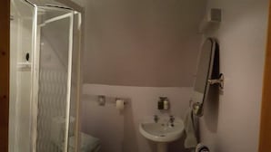 Ein Badezimmer mit Duschkabine aus Glas, einem weißen Waschbecken und einem Spiegel an der Wand.
