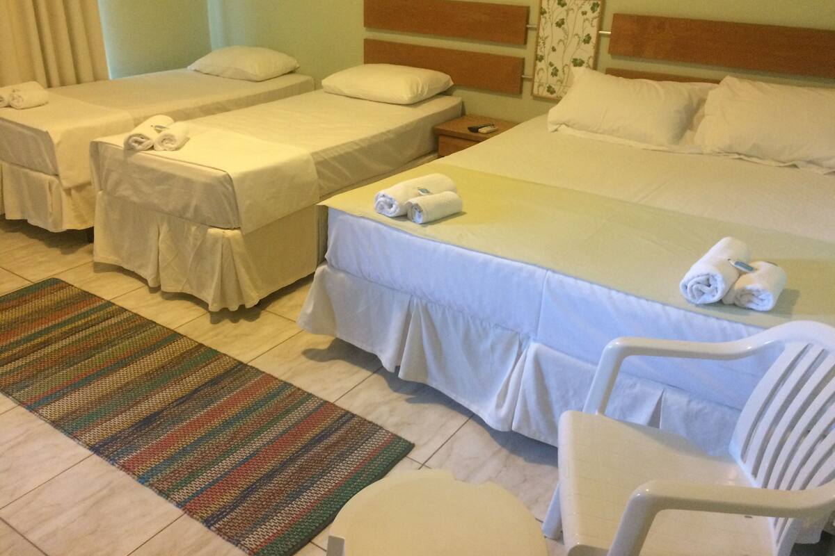 Een hotelkamer met twee eenpersoonsbedden, een groter bed, een klein tafeltje met een afstandsbediening en een stoel.