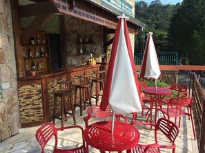 An outdoor bar area with stone walls, wooden bar counter, and red chairs and tables. - Quedasdagua Lazer e Hospedagem (Itu)