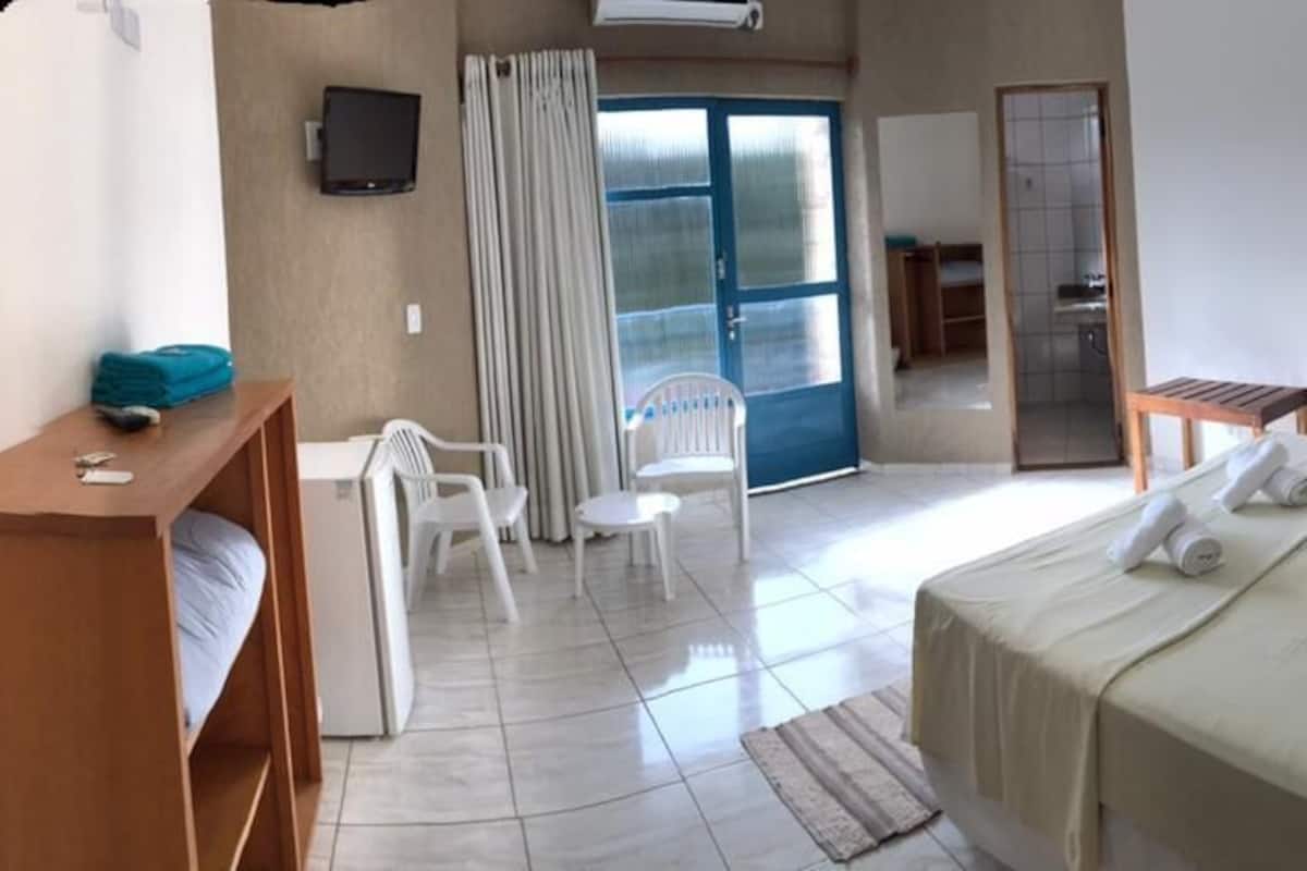 Hotelkamer met een bed, bureau, twee stoelen, kledingkast en een schuifdeur naar een balkon.