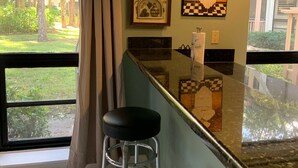 A kitchen with a bar area, a window with a view of greenery, and framed artwork on the wall.