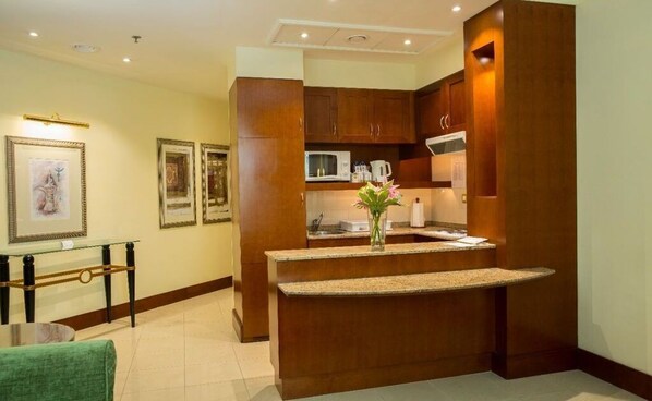Enjoy a compact kitchen with microwave, wooden cabinetry, and a glass shelf.
