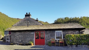 A stone cottage with a red door, a small porch with two wooden chairs, and a garden with flowers. - Field House Bothy - UK12571 (Borrowdale, near Keswick)