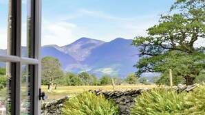 A stone wall with ferns, a wooden fence, and a mountain range in the background. - Field House Bothy - UK12571 (Borrowdale, near Keswick)