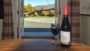 A wine bottle and glass on a table with a view of a rural landscape through an open door. - Field House Bothy - UK12571 (Borrowdale, near Keswick)