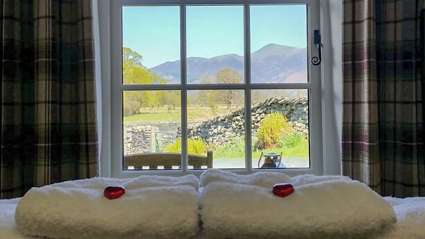 A room with a large window offering a view of a stone wall, trees, and distant mountains. - Field House Bothy - UK12571 (Borrowdale, near Keswick)