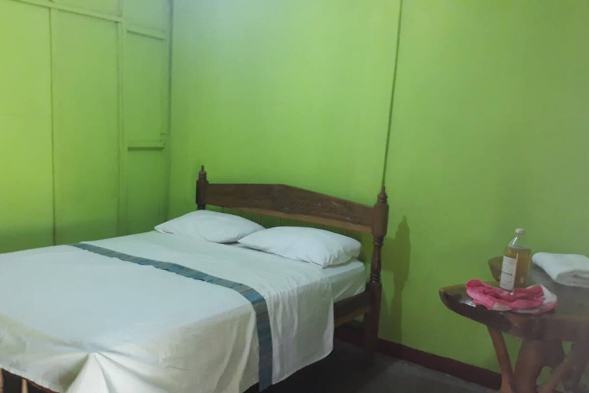 A room with a bed, a small table with a bottle and cloth, and green walls.