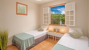 Un dormitorio con dos camas, un escritorio, una ventana con contraventanas, una lámpara colgante y un cuadro en la pared.
