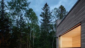 A modern wooden cabin with a hot tub in the center, surrounded by a forest. - Le Littoral : Luxurious Chalet with Pool Sauna Spa & View (La Malbaie)