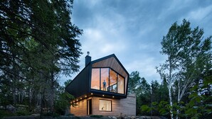 A modern house with large windows, a wooden exterior, and a stone pathway leading to the entrance. - Le Littoral : Luxurious Chalet with Pool Sauna Spa & View (La Malbaie)