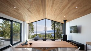 A modern meeting room with a large wooden table, white chairs, and a large window offering a scenic view. - Le Littoral : Luxurious Chalet with Pool Sauna Spa & View (La Malbaie)