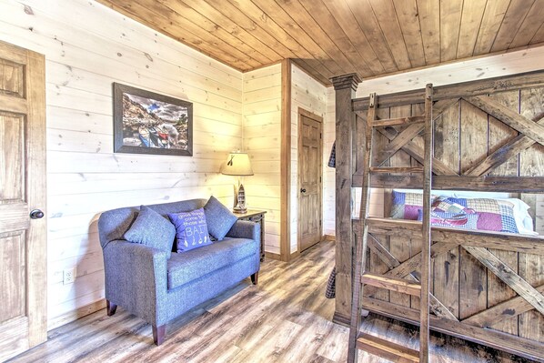 A cozy room with wooden walls, a sofa, a ladder, and a bed with a quilt.