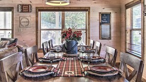 A wooden cabin dining area with a table set for six, surrounded by chairs, a central flower arrangement, and a sign indicating all decks are out.