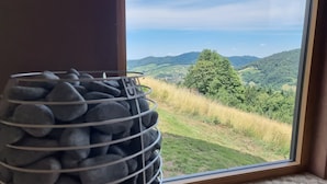 A window with a view of a green landscape and a metal basket with rocks.
