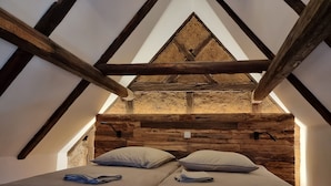 A cozy attic bedroom with a sloped ceiling, wooden beams, and a rustic stone wall.
