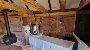 A rustic kitchen with exposed wooden beams, a brick wall, a white bar counter, and two wooden stools.