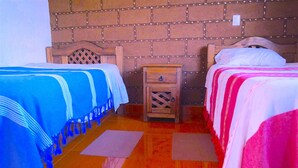 Una stanza con due letti, un comodino in legno e un muro in mattoni.