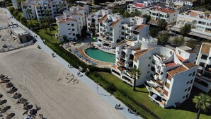 Een kusthotel met een centraal gelegen zwembad, meerdere balkons en een strandgedeelte.