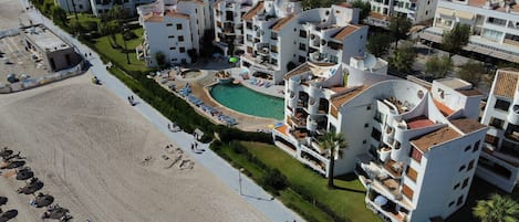 A coastal hotel with a central swimming pool, multiple balconies, and a beach area.