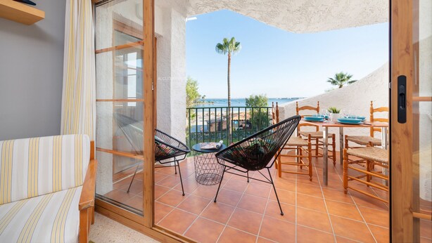 Een balkon met een tafel en stoelen, uitzicht op zee, en een palmboom.