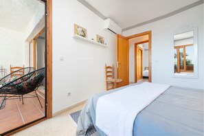 A bedroom with a bed, a chair, a wooden door, and a window. - LORTAL apartment on the first line of the beach with swimming pools (Alcúdia)
