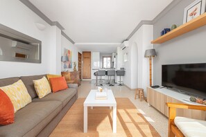 Un salon moderne avec un canapé, une table basse, un téléviseur et une cuisine en arrière-plan.